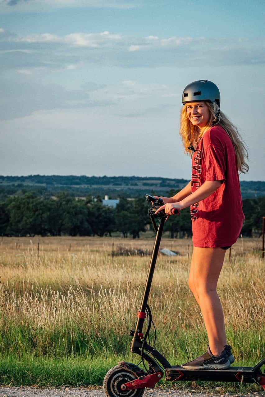 Ein junges Mädchen mit Helm fährt mit einem E-Scooter auf einer Landstraße.